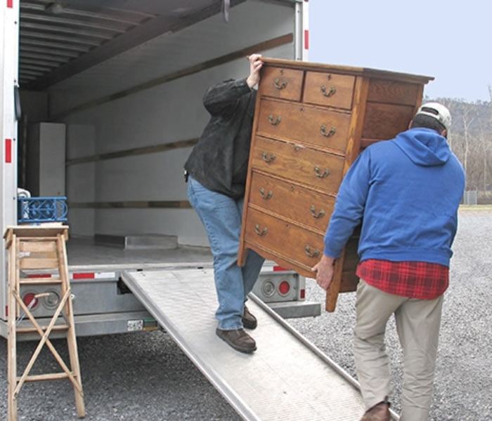 Movers carrying a wooden dresser up the ramp into a moving truck
