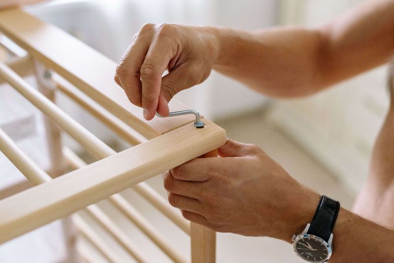 Hands tightening a bolt with an Allen key while assembling a wooden bed frame