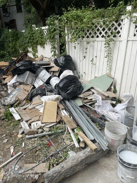 Pile of scrap metal siding, pipes and debris ready for removal beside a fence
